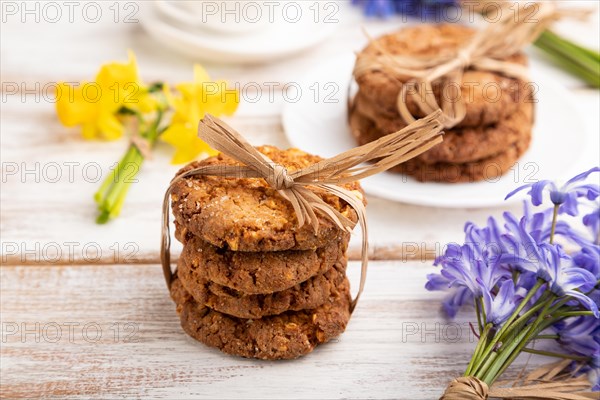 Oatmeal cookies with spring snowdrop flowers bluebells, narcissus and cup of coffee on white wooden