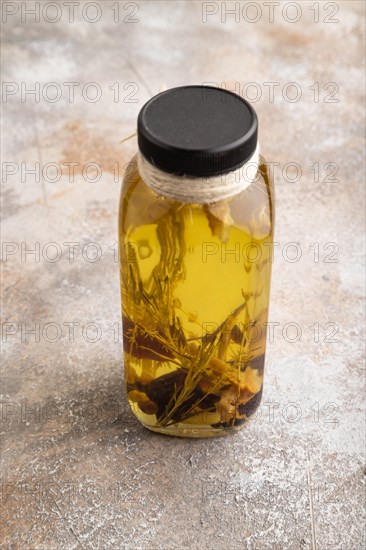 Sunflower oil in a glass jar with various herbs and spices, lavender, sesame, rosemary on a brown