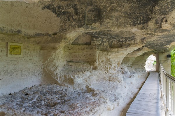 A walkway leads through a cave entrance, accompanied by information signs, cells of the monks,