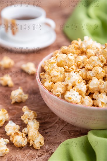 Popcorn with caramel in ceramic bowl on brown concrete background and green textile. Side view,