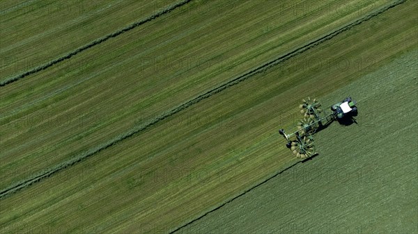 Farmer cutting grass to straight rows with tractor and large roundabout rake, drone shot, Upper