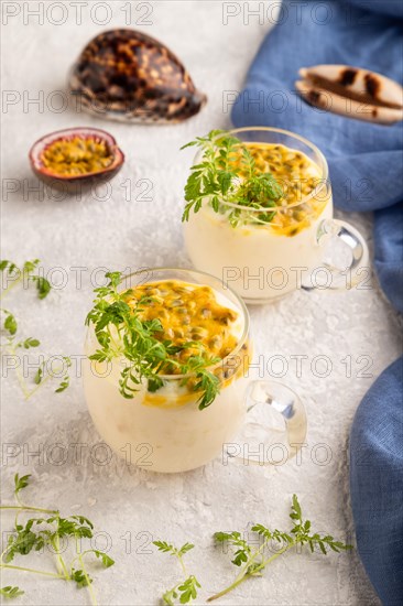 Yogurt with passionfruit and marigold microgreen in glass on gray concrete background with blue