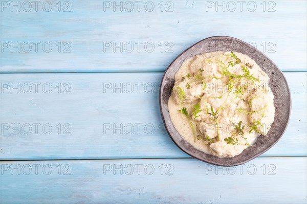 Stewed chicken fillets with coconut milk sauce and mizuna cabbage microgreen on blue wooden