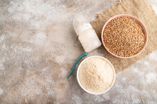 Powdered milk and buckwheat baby food mix, infant formula, pacifier, bottle, spoon on brown