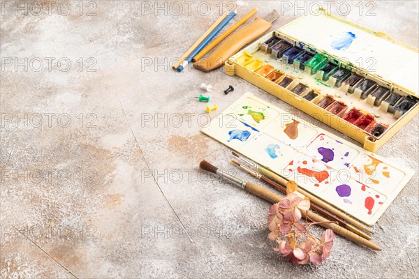 Drawing accessories set: brushes, pencils, watercolor on brown concrete background. Side view, copy