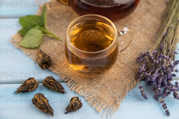 Red tea with herbs in glass on blue wooden background and linen textile. Healthy drink concept.