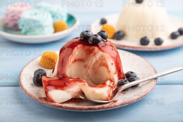 White milk jelly with blueberry jam on blue wooden background and blue linen textile. side view,