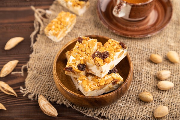 Traditional candy nougat with nuts and sesame with cup of green tea on brown wooden background and
