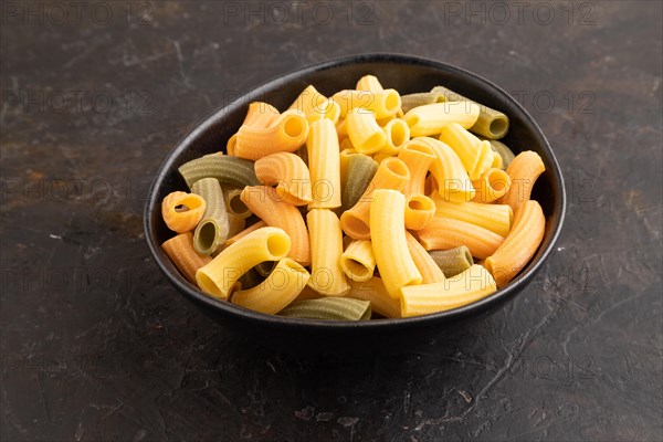 Rigatoni colored raw pasta with tomato, eggs, spices, herbs on black concrete background. Side