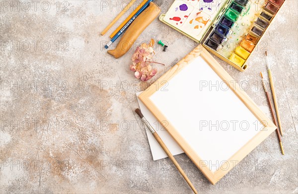 Drawing accessories set: brushes, pencils, watercolor, frame on brown concrete background. Top