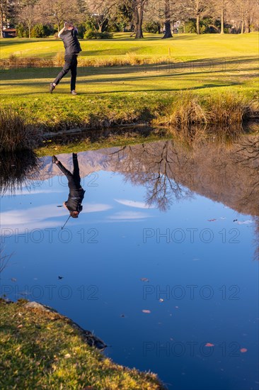 Male Golfer Reflected in a Water Pond and Hitting the Golf Ball on Fairway on Golf Course with