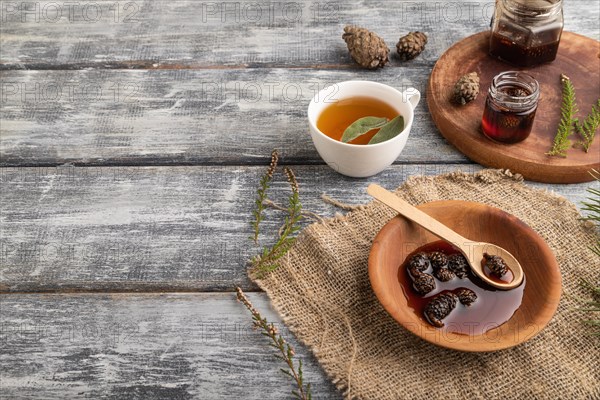 Pine cone jam with herbal tea on gray wooden background and linen textile. Side view, copy space