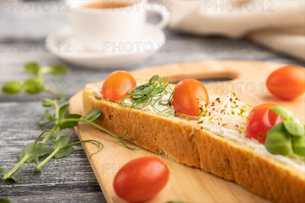 Long white bread sandwich with cream cheese, tomatoes and microgreen on gray wooden background and
