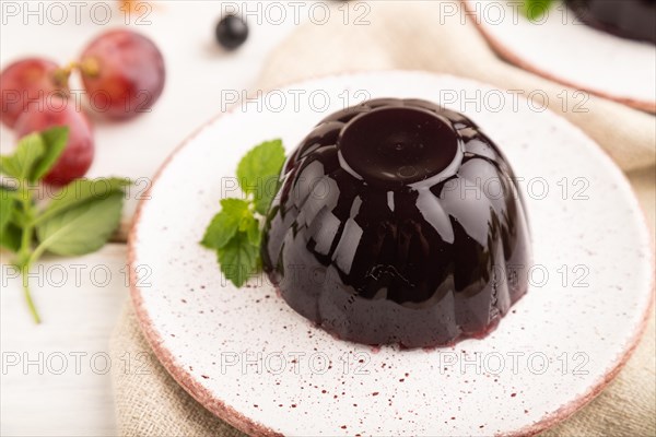 Black currant and grapes jelly on white wooden background and linen textile. side view, close up,