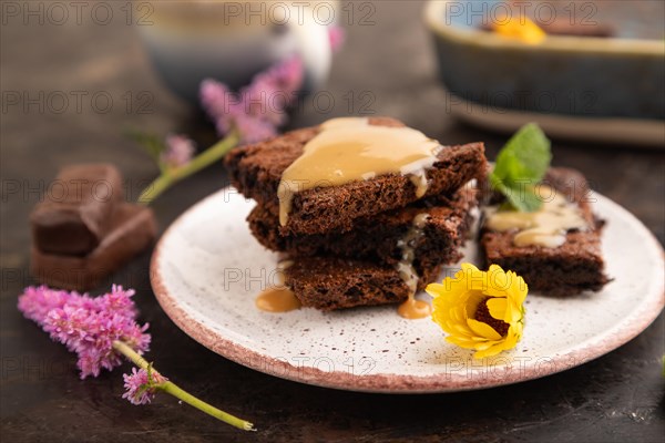 Chocolate brownie with caramel sauce with a cup of coffee on black concrete background. side view,