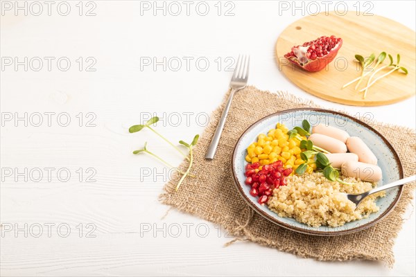 Mixed quinoa porridge, sweet corn, pomegranate seeds and small sausages on white wooden background.