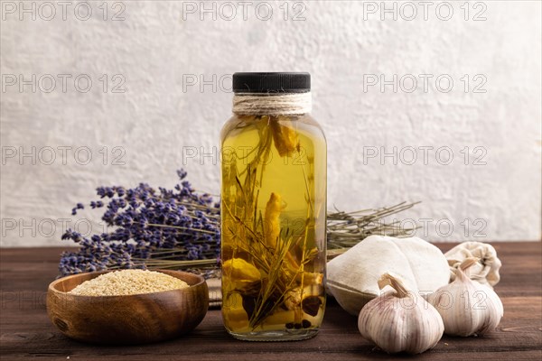 Sunflower oil in a glass jar with various herbs and spices, lavender, sesame, rosemary on a brown