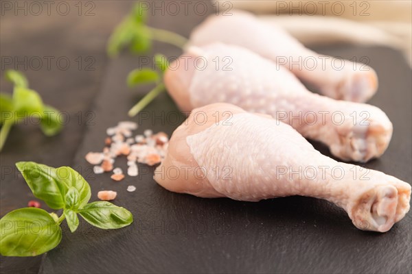 Raw chicken legs with herbs and spices on a black slate cutting board on a black concrete