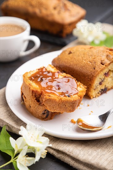 Homemade cake with raisins, almonds, soft caramel and a cup of coffee on a black concrete