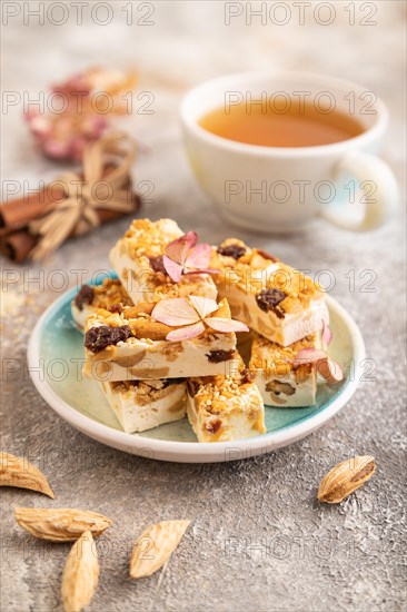 Traditional candy nougat with nuts and sesame with cup of green tea on brown concrete background.
