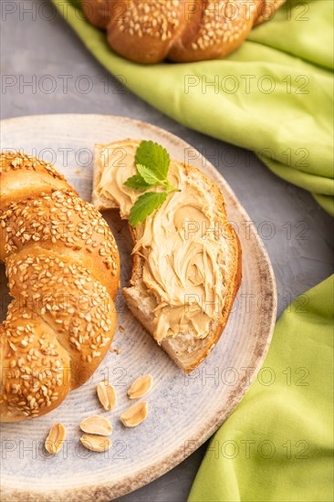 Homemade sweet bun with peanut butter and cup of coffee on a gray concrete background and green