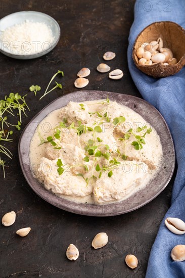 Stewed chicken fillets with coconut milk sauce and rucola microgreen on black concrete background