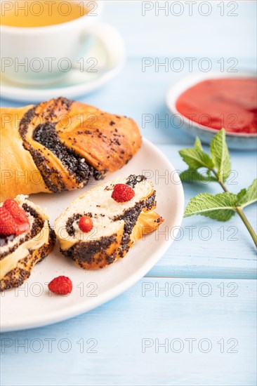 Homemade sweet bun with strawberry jam and cup of green tea on a blue wooden background. side view,