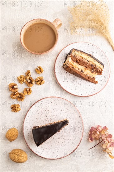 Chocolate biscuit cake with caramel cream and walnuts, cup of coffee on gray concrete background.