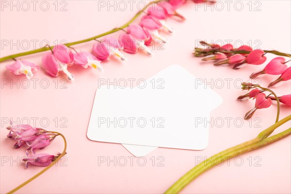 White business card with pink dicentra, broken heart flowers on pink pastel background. side view,