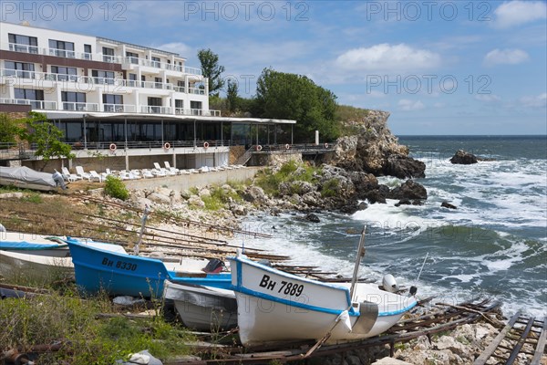 A coastal hotel overlooking the moving sea, surrounded by boats and rocky landscape, harbour and