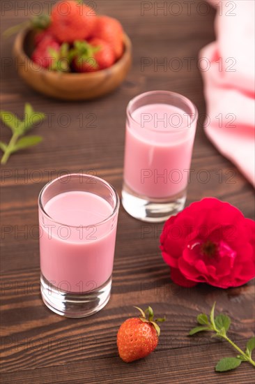Sweet strawberry liqueur in glass on a brown wooden background and pink textile. side view, close