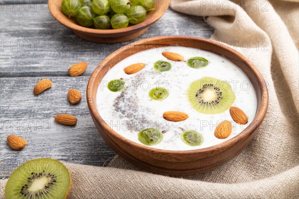 Yogurt with kiwi, gooseberry, chia and almonds in wooden bowl on gray wooden background and linen