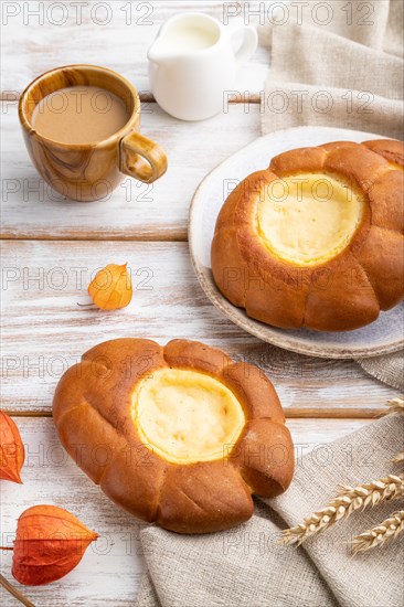 Sour cream bun with cup of coffee on a white wooden background and linen textile. Side view, close