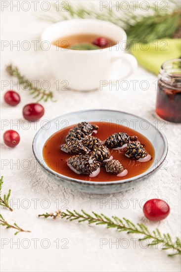 Pine cone jam with herbal tea on gray concrete background and green linen textile. Side view,