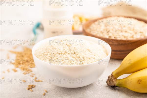 Powdered milk and oatmeal, banana baby food mix, infant formula, pacifier, bottle, spoon on gray