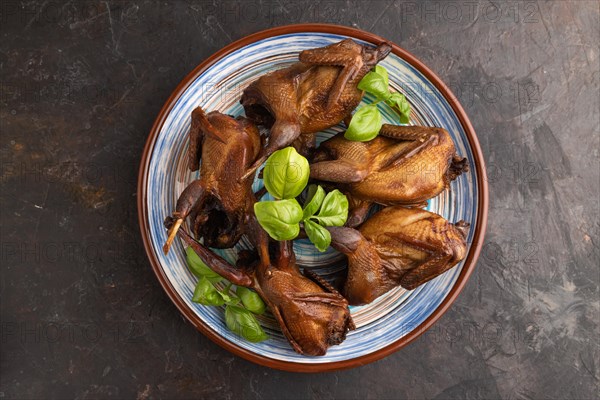 Smoked quails with herbs and spices on a ceramic plate on a black concrete background. Top view,
