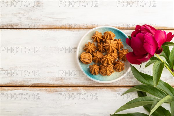 Homemade soft caramel fudge candies on blue plate on white wooden background, peony flower