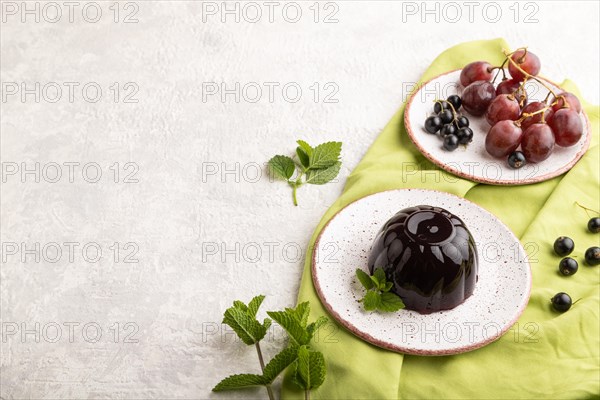 Black currant and grapes jelly on gray concrete background and green linen textile. side view, copy