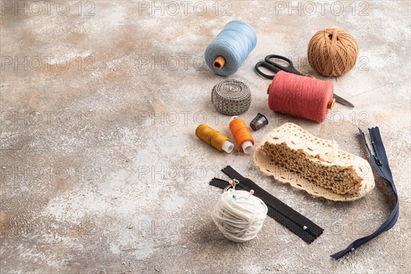 Sewing accessories: scissors, thread, thimbles, braid on brown concrete background. Side view, copy