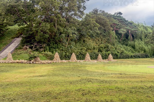 Row of cairn (towers of stack stones) in front of treeline with stairs up side of hill on left in