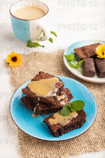 Chocolate brownie with caramel sauce with a cup of coffee on gray concrete background and linen