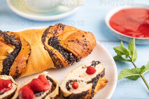 Homemade sweet bun with strawberry jam and cup of green tea on a blue wooden background. side view,