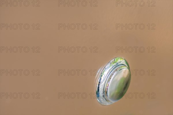 Closeup of silver metallic push button switch used to turn on power to machine on soft brown