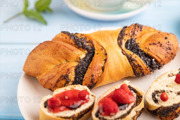 Homemade sweet bun with strawberry jam and cup of green tea on a blue wooden background. side view,