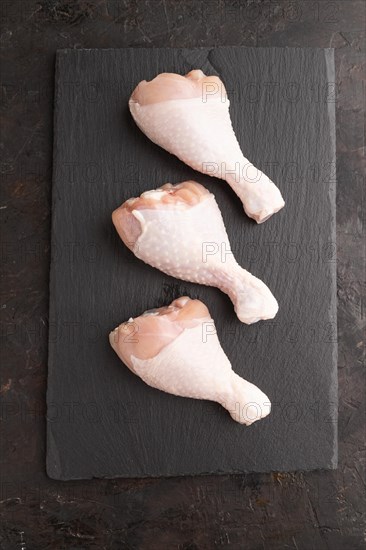 Raw chicken legs on a black slate cutting board on a black concrete background. Top view, flat lay,