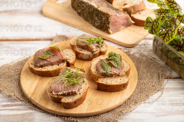 Bread sandwiches with jerky salted meat, sorrel and cilantro microgreen on white wooden background