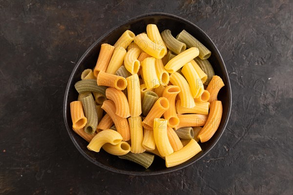 Rigatoni colored raw pasta with tomato, eggs, spices, herbs on black concrete background. Top view,