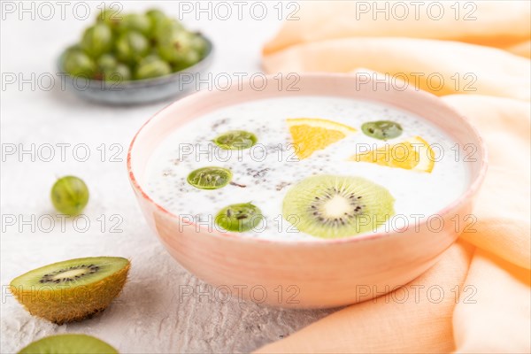 Yogurt with kiwi, gooseberry, chia in ceramic bowl on gray concrete background and orange linen