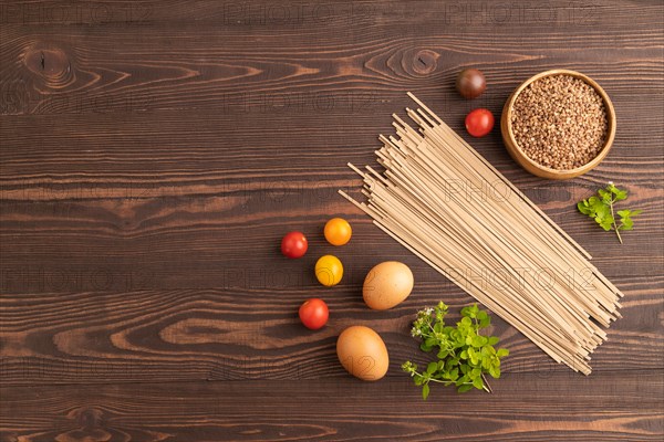 Japanese buckwheat soba noodles with tomato, eggs, spices, herbs on brown wooden background. Top