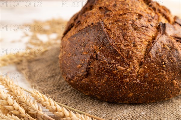 Fresh homemade golden grain bread with ears of wheat and rye on white wooden background and linen